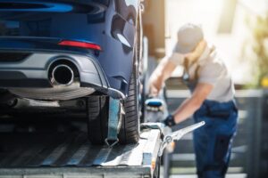 Professional auto transport worker securing a blue car onto a flatbed trailer for cross-country car shipping.