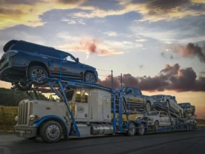 A multi-car carrier truck loaded with SUVs and pickups driving on a highway during a sunset.